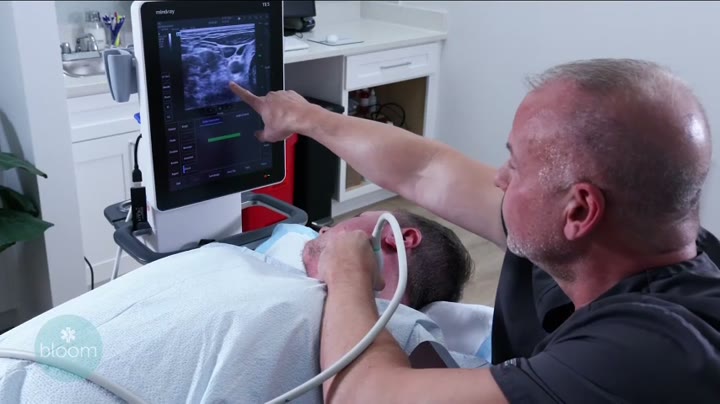 Dr. Michael Meighen points at the ultrasound monitor beside a patient on the treatment table